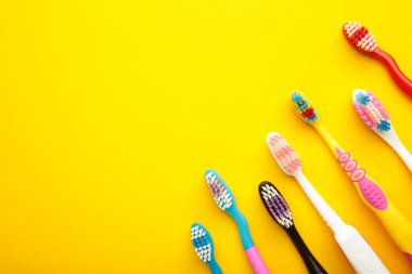 Colorful toothbrushes on yellow background with copy space. Top view