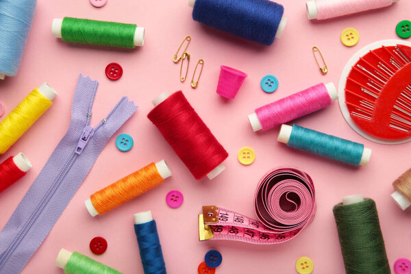 Sewing supplies on pink background: sewing thread, scissors, a large spool of thread, pieces of cloth, needles,centimeter, buttons. Top view