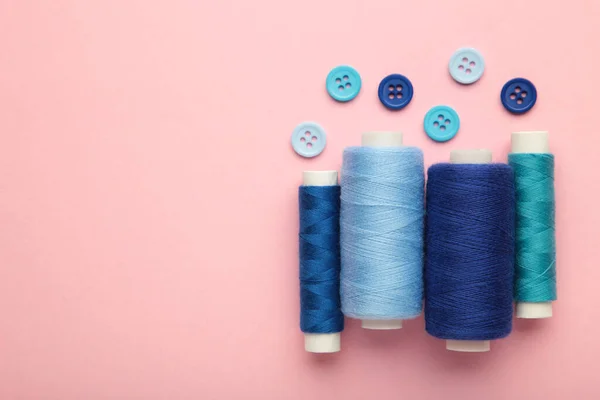 Blue cotton yarns on rolls for sewing on pink background. Top view