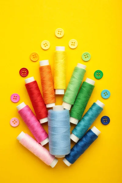 Colorful buttons with colorful thread on yellow background. Top view