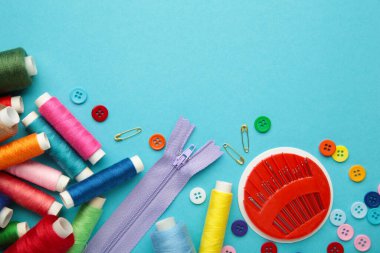 Mavi arka planda dikiş malzemeleri: dikiş ipliği, makas, büyük bir makara iplik, kumaş parçaları, iğneler, santimetre, düğmeler. Üst görünüm