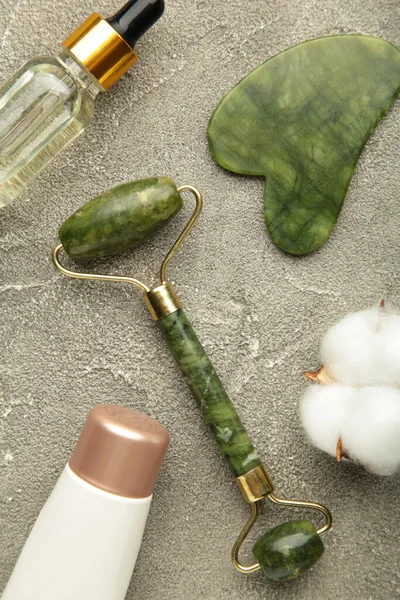 Green jade roller and gua sha stone for facial massage and on grey background. Home beauty and selfcare accessories. Face roller for anti age wrinkle treatment. Vertical photo