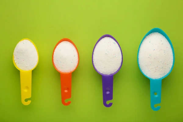 Measuring scoop with laundry powder on green background. Top view