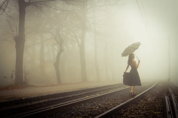 Femeia frumoasă cu rochie neagră și umbrelă pe o pistă de tren — Fotografie, imagine de stoc