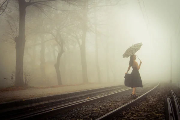 Belle femme avec robe noire et parapluie sur une voie ferrée — Photo