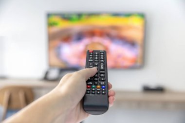 Uzaktan kumandalı adam televizyon izleyip uzaktan kumanda kullanarak düğmeye basıyor.