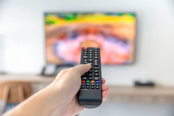 Uzaktan kumandalı adam televizyon izleyip uzaktan kumanda kullanarak düğmeye basıyor.
