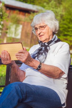 Gülümseyen yaşlı kadın dışarıda dijital tablet kullanıyor. Yaşlılar tarafından teknoloji kullanımı.