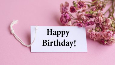 Beautiful Pink Dried Roses and Happy Birthday Note on a Pink Background