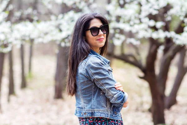 春に咲く木々の上に黒いサングラスの屋外の美しい若いブルネットの女性背景 — ストック写真