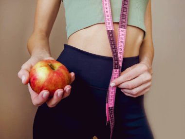 Elinde mezura ve elma olan sıska, tanınmayan bir kadın. Kilo kaybı ve sağlıklı yaşam tarzı kavramı.