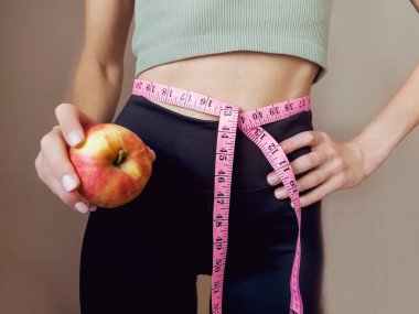 Elinde mezura ve elma olan sıska, tanınmayan bir kadın. Kilo kaybı ve sağlıklı yaşam tarzı kavramı.