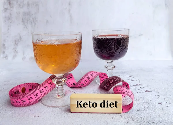 Glasses of wine and rose with measuring tape and keto diet message on wooden cubes