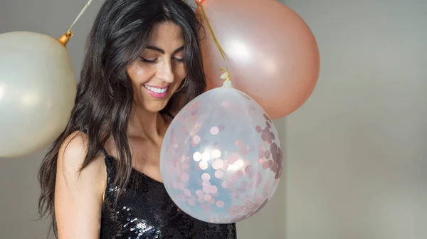 Beautiful woman in black shiny dress holding party balloons and smiling . Portrait with copy space