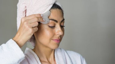 Gua Sha Rose Kuvars Taşı 'nı yüz masajı için kullanan güzel bir kadın. Günlük Gua Sha Masaj Programı 