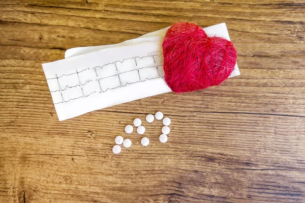 Red heart with pills and cardiogram on wooden background