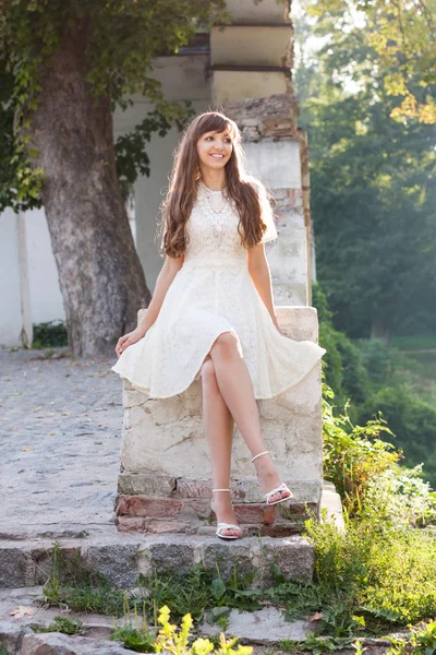 Slim girl sitting on the ruins in the park and smiling — Stock Photo, Image