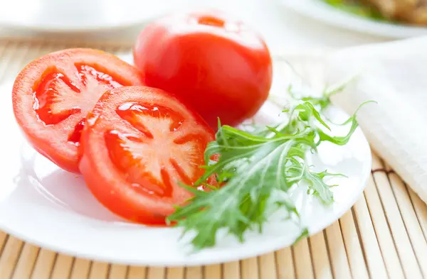 Ripe tomato on a white plate and salad leaves — Stock Photo, Image