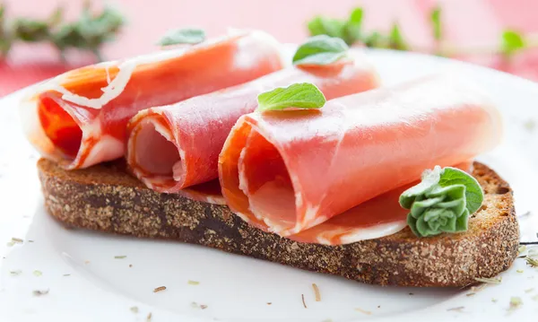 Slices of ham wrapped in a roll on a piece of bread — Stock Photo, Image