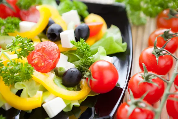 Salad with fresh vegetables on a black plate — Stock Photo, Image