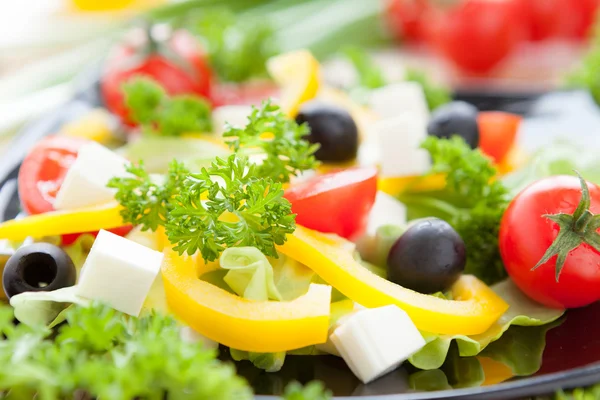 Salad with fresh vegetables and feta on a black plate — Stock Photo, Image