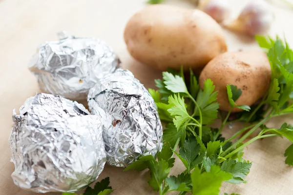 Three potatoes in foil and a bunch of parsley — Stock Photo, Image