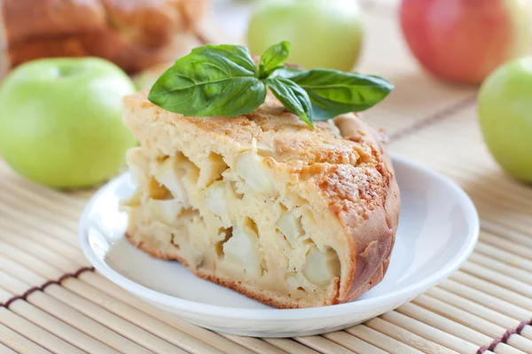 Кусочек яблочного пирога на фоне яблок — стоковое фото