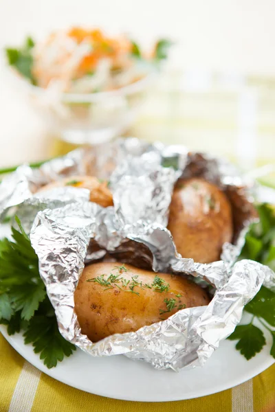 Potatoes in foil not a white plate and a bowl of salad — Stock Photo, Image