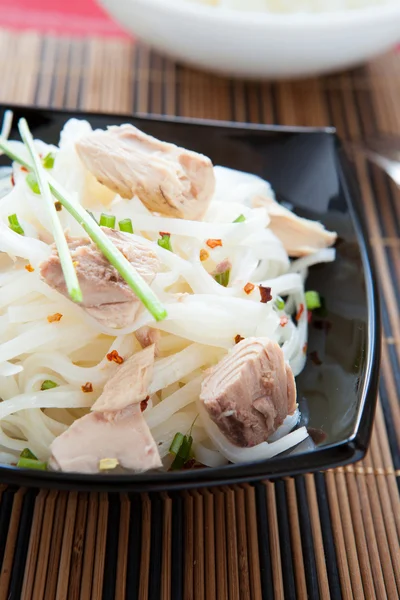 appetizing rice noodles with chunks of tuna in a black bowl