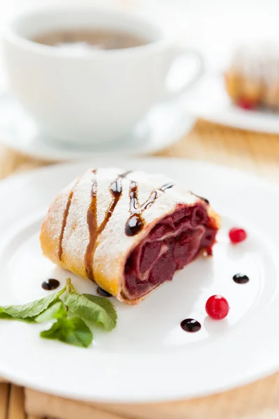 Cherry strudel on white plate and a cup of tea — Stock Photo, Image