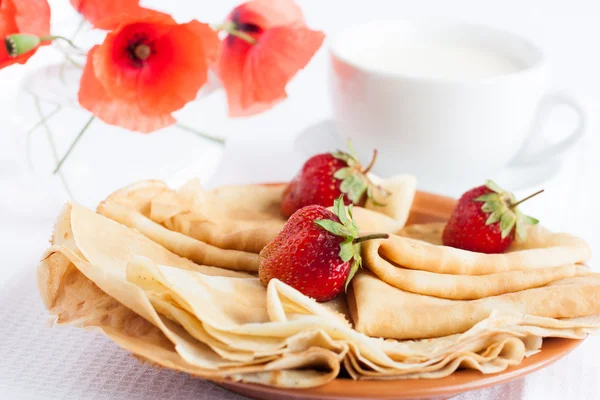 Ruddy pancakes, strawberries on top and a cup of milk — Stock Photo, Image
