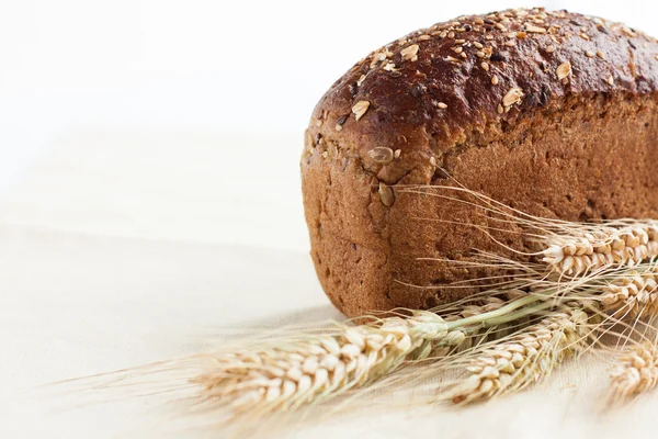 Loaf whole wheat bread and wheat ears — Stock Photo, Image