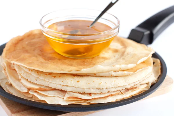 Round pancakes in a frying pan and honey — Stock Photo, Image