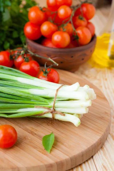 El manojo de la cebolla verde en la tabla de cortar y los tomates pequeños — Foto de Stock