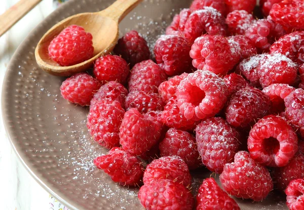Juicy raspberries on a plate and wooden spoon — Stock Photo, Image