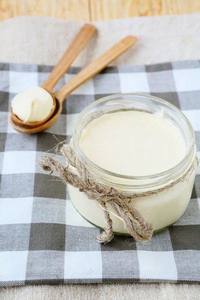 Crema agria en un frasco y cucharas de madera — Foto de Stock