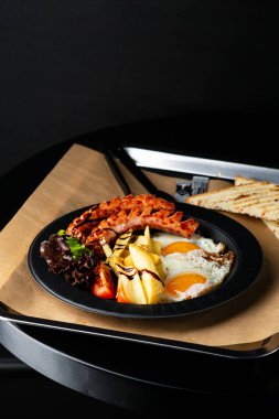 Sosisli ve salatalı kahvaltı yumurtaları karanlık masaya yakın.