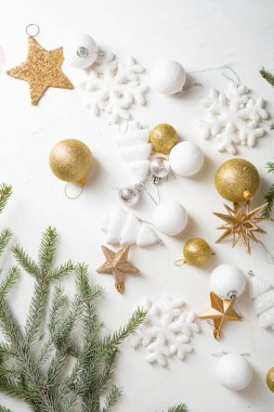 Golden and white Christmas tree decorations on light surface and green branches top view