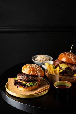 Two tasty cheeseburger and potatoes french fries on dark table copy space