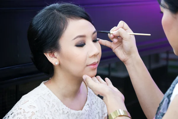 Make-up artist applying cosmetics on a beautiful young asian lad