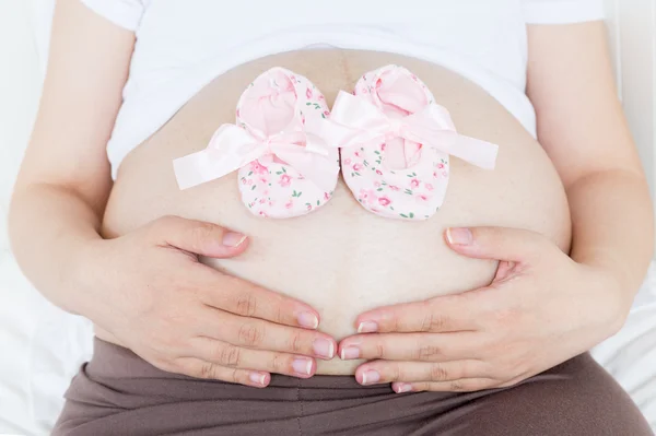 Pregnant belly with a pair of pink shoes — Stock Photo, Image