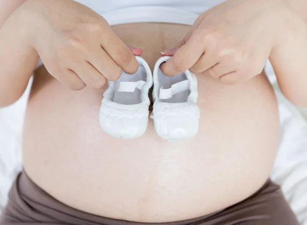 Pregnant belly with a pair of white shoes — Stock Photo, Image
