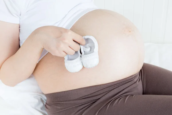 Pregnant belly with a pair of white shoes — Stock Photo, Image