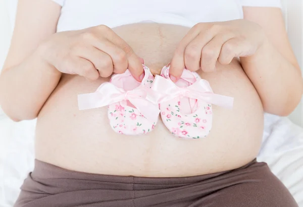 Pregnant belly with a pair of pink shoes — Stock Photo, Image