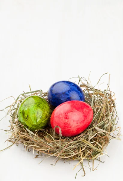 Œufs de Pâques dans le nid de foin sur bois blanc — Photo