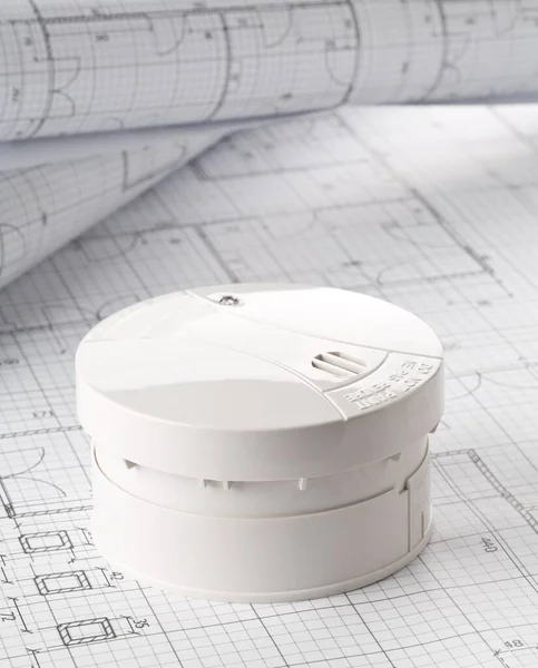 Smoke detector or fire alarm sensor on white architectural plans background, house safety or security concept, copy space, vertical view
