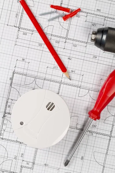 Smoke detector or fire alarm sensor on white architectural plans background with drill, screwdriver and screws, house safety or security concept, flat lay top view from above, vertical layout