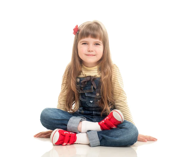 Cute little girl wearing jeans overall sitting on the floor and — Stock Photo, Image