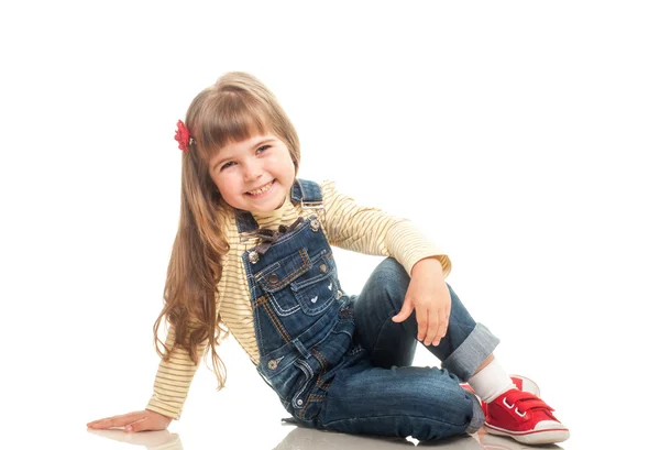 Söt liten flicka klädd i jeans övergripande sitter på golvet och — Stockfoto
