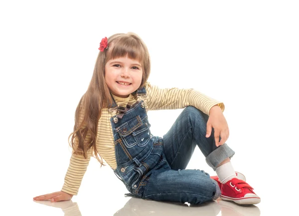 Cute little girl wearing jeans overall sitting on the floor and — Stock Photo, Image